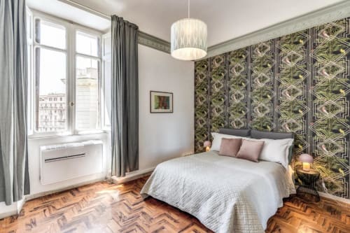 Elegante camera da letto in appartamento romano con carta da parati verde decorata, pavimenti in spina di pesce e vista sulla città