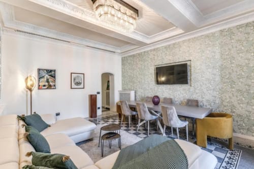 Elegante appartamento romano con divano crema, tavolo da pranzo, carta da parati decorata, soffitto a cassettoni e TV a schermo piatto