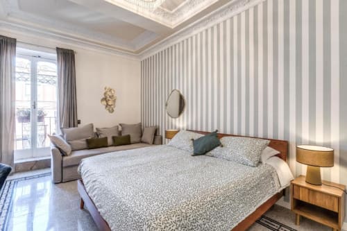 Camera da letto elegante a Roma con letto in legno, carta da parati rigata, zona salotto e balcone con vista sulla città