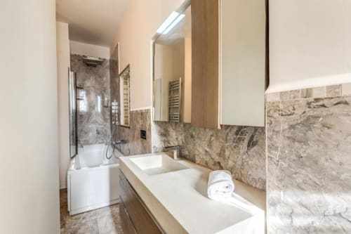 Bagno moderno nell'appartamento di Emily a Roma con doppi lavandini, rivestimento in marmo, doccia a fondo vasca e scaldasalviette
