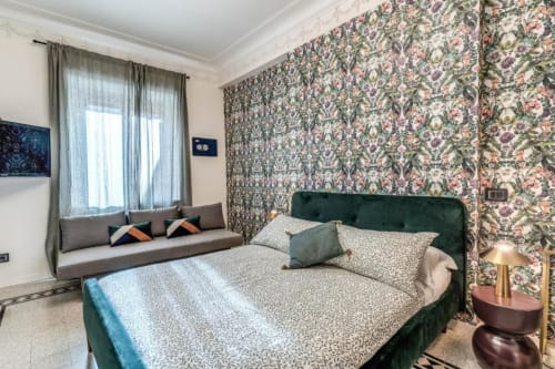 Camera da letto moderna con letto rivestito in verde, carta da parati floreale, finestra-seduta e vista sulla città nell'appartamento di Emily a Roma