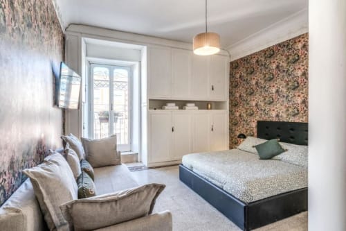 Camera da letto moderna nell'appartamento di Emily a Roma, con letto matrimoniale, carta da parati floreale, porta-finestra e arredi contemporanei.