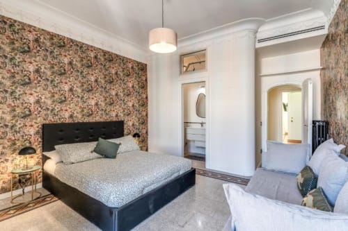 Camera da letto moderna nell'appartamento Emily Rome con carta da parati floreale, letto nero, divano e bagno ensuite