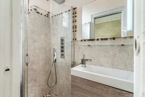 Bagno moderno con doccia in marmo, lavabo bianco e dettagli decorativi in piastrelle nell'appartamento di Emily a Roma