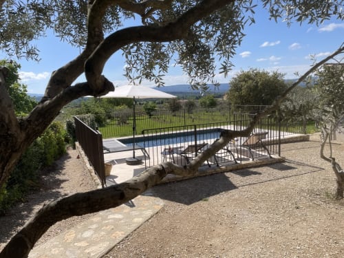 Villa in Gordes mit Pool, Olivenbäumen, Liegestühlen unter Sonnenschirm und Blick auf die provenzalische Landschaft