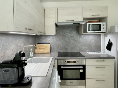 Kitchenette moderne à LOCADIGNE Digne-les-Bains : armoires blanches, crédence grise, four, micro-ondes et cafetière