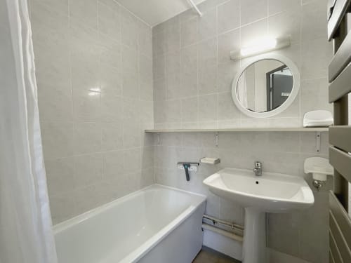Salle de bain moderne à l'hôtel LOCADIGNE à Digne-les-Bains avec carrelage blanc, baignoire, lavabo sur colonne et miroir rond