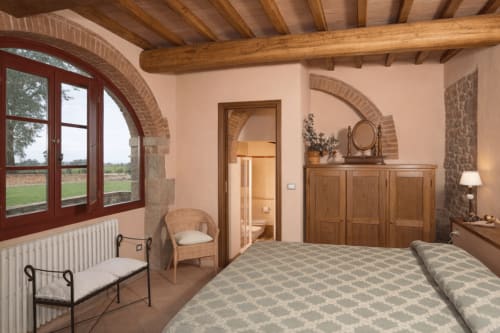 Camera da letto rustica a Villa Olena a Reggello con travi a vista, archi in mattoni e vista sulla campagna