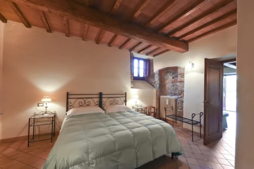 Camera Gretaio a Villa Olena a Reggello con letto in ferro battuto, travi a vista, dettagli in pietra e vista sul giardino