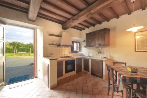Cucina Gretaio a Villa Olena con travi in legno, vista sul giardino e zona pranzo a Reggello
