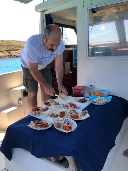 Uomo che prepara piatti di degustazione con frutti di mare freschi a bordo di un'imbarcazione da pesca presso Pescaturismo Lia a Stintino, Italia