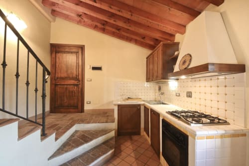 Cucina della sala Morgone a Villa Olena a Reggello con travi in legno, cucina a gas e rivestimento in piastrelle color crema