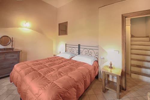Camera luminosa di Villa Olena con biancheria corallo, testata in metallo, mobili in legno e porta vista giardino