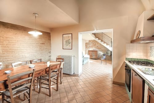 La sala Pianuglia di Villa Olena a Reggello presenta una zona cucina-pranzo aperta con pavimenti in cotto, muri in laterizio e legno