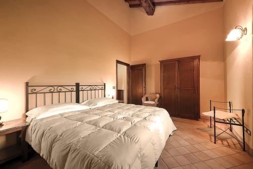 Ampia camera da letto a Villa Olena a Reggello con letto in ferro battuto, pavimenti in cotto e illuminazione calda