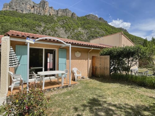 Pavillon de l'aparthotel Vallon des Sources avec volets turquoise, terrasse meublée et falaises rocheuses spectaculaires
