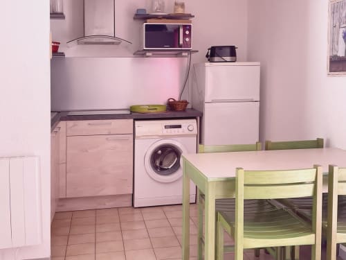 Cuisine rose avec lave-linge, cuisinière, micro-ondes, réfrigérateur et salle à manger de l'appartement Vallon des Sources