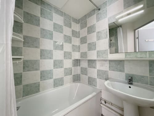 Salle de bains moderne du Pavillon 84 LOCADIGNE avec carrelage damier bleu-vert et blanc, baignoire, lavabo sur colonne, miroir et douche