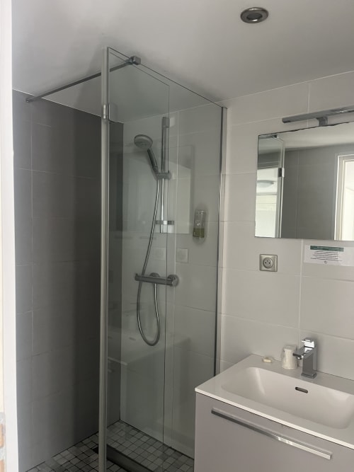 Modern bathroom with walk-in shower, white sink, and mirror at Hotel Flots d'Azur Nice