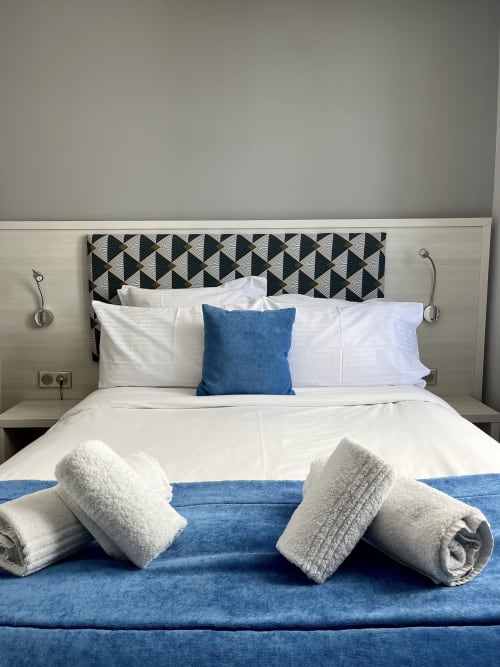 Chambre élégante de l'Hôtel Flots d'Azur à Nice avec serviettes roulées, coussin bleu et tête de lit géométrique