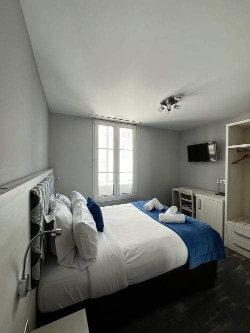 Modern hotel bedroom at Hotel Flots d'Azur in Nice with double bed, sea view balcony, flat-screen TV, and white furnishings