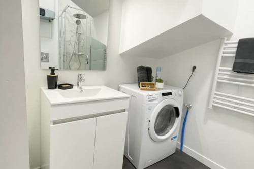 Salle de bains moderne et buanderie de l'appartement Volta aux Logis d'Emma avec lavabo blanc, miroir et lave-linge