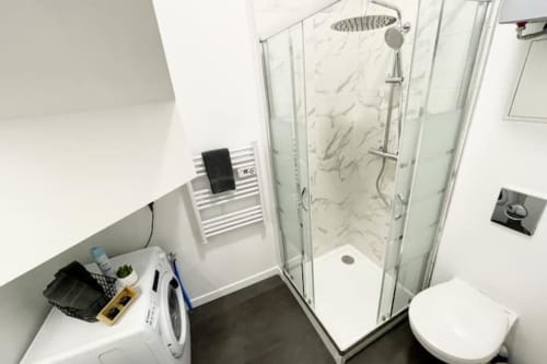 Salle de bain moderne de l'appartement Les Logis d'Emma avec douche à l'italienne, toilettes, lave-linge et sèche-serviettes électrique