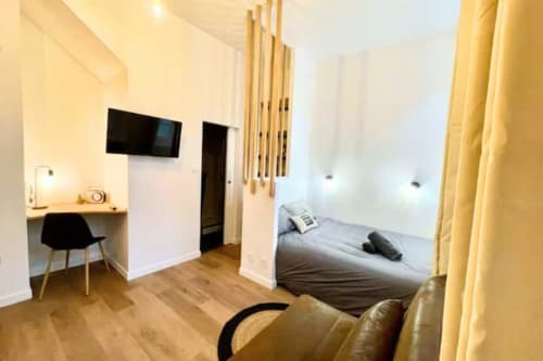 Studio moderne aux Logis d'Emma avec lit, bureau avec chaise, TV murale et rideaux jaunes