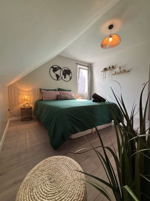 Chambre mansardée moderne aux Logis d'Emma avec literie verte, parquet, luminaire suspendu et vue sur les montagnes