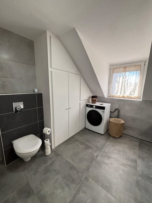 Salle de bains moderne avec toilettes, lave-linge et rangements dans l'appartement Le Col'Vert aux Logis d'Emma