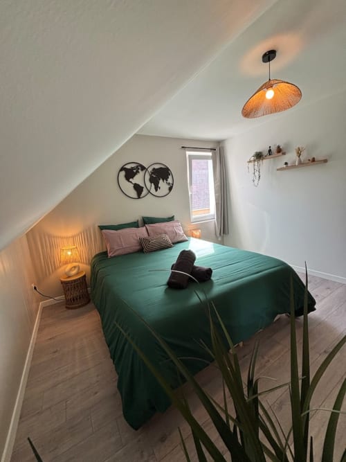 Chambre mansardée moderne avec literie verte, luminaire suspendu tressé et carte du monde aux Logis d'Emma