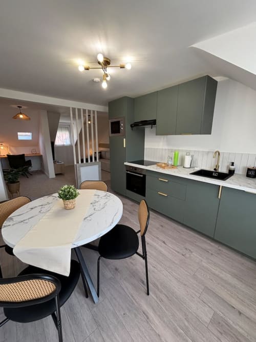 Cuisine et salle à manger modernes de l'appartement Le Col'Vert aux Logis d'Emma avec armoires vert sauge et table en marbre