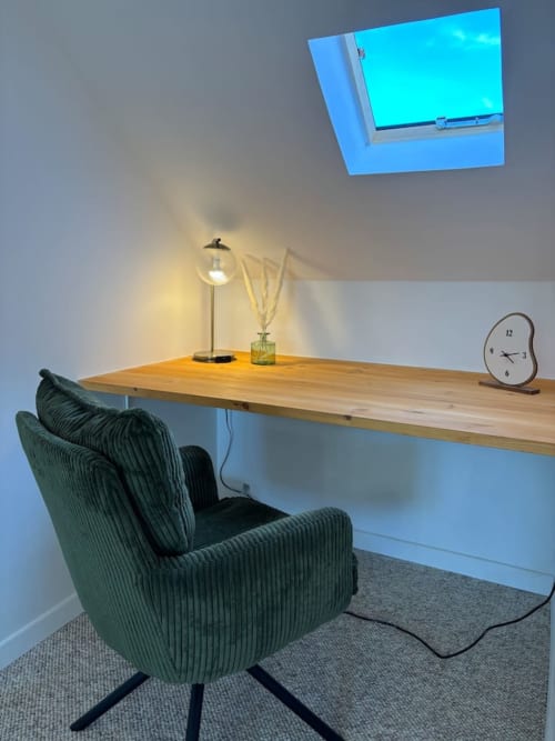 Espace de travail moderne à l'appartement Le Col'Vert avec bureau en bois, chaise verte, lampe de bureau, horloge et puits de lumière