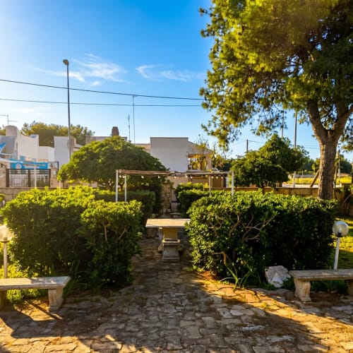 Lussureggiante giardino interno a My Home Apulia a Veglie con siepi verdi, vialetto in pietra e architettura mediterranea