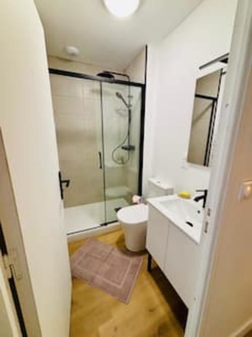 Salle de bain moderne de l'appartement Midori aux Logis d'Emma avec douche vitrée, vasque blanche et parquet