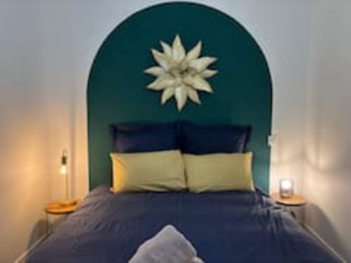 La chambre Midori aux Logis d'Emma avec tête de lit cintrée bleu-vert, oreillers crème, parure bleu marine et décoration étoilée