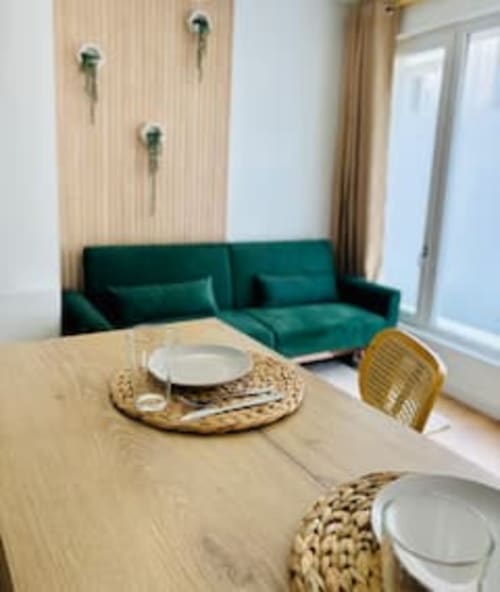 Séjour Midori avec canapé bleu-vert, table en bois, couverts dressés et lumière naturelle aux Logis d'Emma