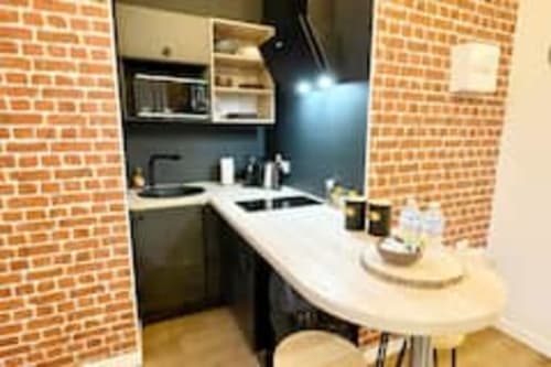 Petite cuisine moderne de l'appartement Volta aux Logis d'Emma : meubles noirs, plan de travail blanc et murs en briques apparentes