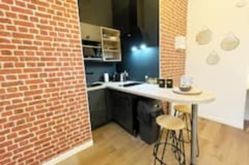 Cuisine moderne de l'appartement Volta aux Logis d'Emma avec mur de briques, mobilier foncé, plan de travail blanc et bar