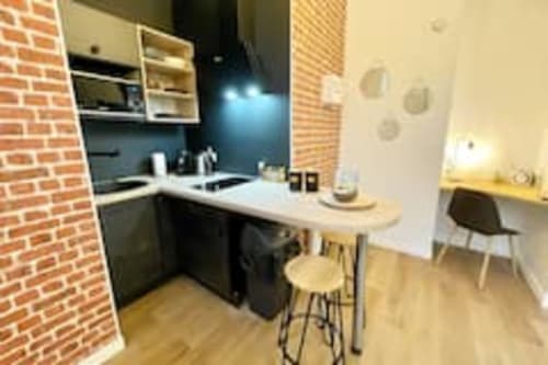 Cuisine moderne de l'appartement Volta aux Logis d'Emma avec meubles noir et blanc, mur de brique et salle à manger