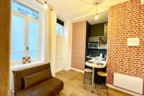 Studio moderne avec murs en briques apparentes, kitchenette, bureau et fenêtre vue sur la ville aux Logis d'Emma