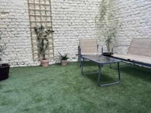 Jardin de l'appartement Terravita aux Logis d'Emma avec transats, mur de briques blanches couvert de lierre et plantes en pots