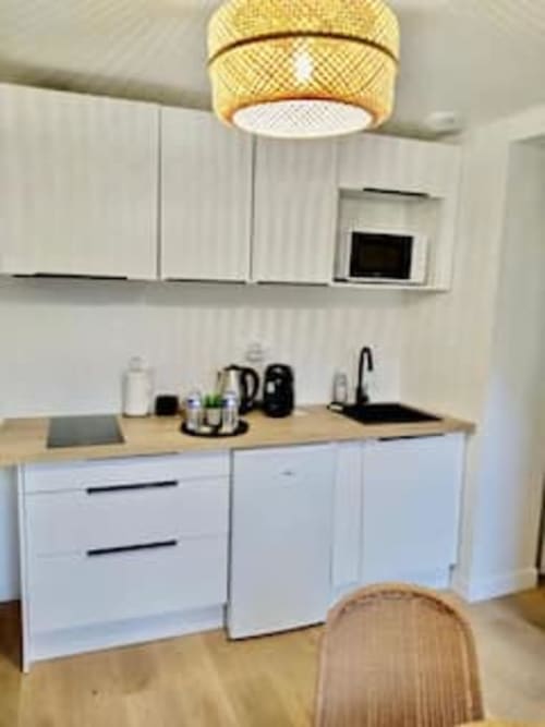 Kitchenette moderne de l'appartement Terravita aux Logis d'Emma, avec armoires blanches, plan de travail en bois et plafond en laiton