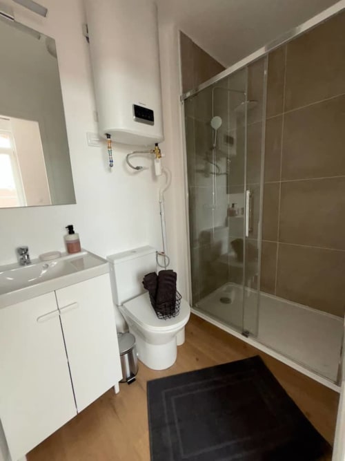 Salle de bain moderne de l'appartement Yogi des Logis d'Emma avec douche, vasque blanche et sèche-serviettes électrique.