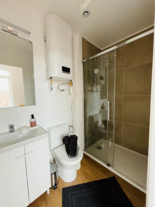 Salle de bain moderne aux Logis d'Emma avec lavabo blanc, douche à l'italienne, toilettes et revêtement de bois