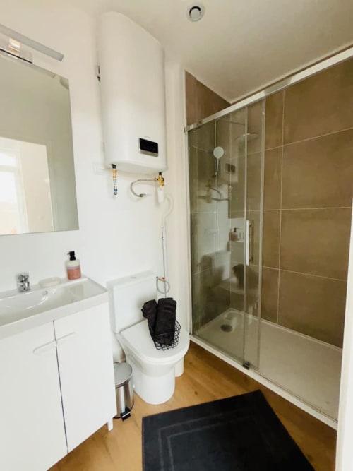 Salle de bains moderne des Logis d'Emma avec lavabo blanc, toilettes, douche vitrée carrelage marron, miroir
