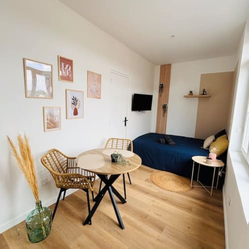 Studio moderne aux Logis d'Emma avec table à manger en bois, lit bleu, œuvre murale et télévision écran plat