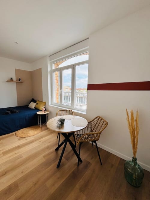 Studio moderne aux Logis d'Emma avec lit bleu, table ronde et vue sur l'océan par grandes fenêtres