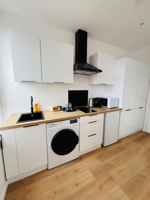 Cuisine moderne de l'appartement Le Yogi aux Logis d'Emma avec armoires blanches, comptoirs en bois, électroménagers noirs et
