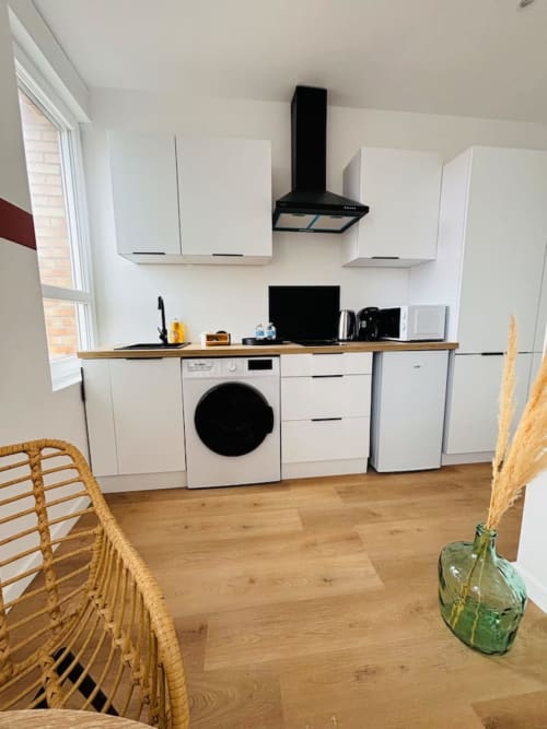 Kitchenette moderne de l'appartement Yogi aux Logis d'Emma avec meubles blancs, lave-linge et plan de travail en bois.